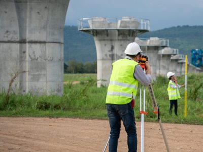 Survey team is working with a theodolite and road construction plans. Civil engineers are taking measurements with surveying tools during the construction.